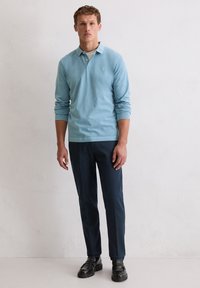 Lichtblauw poloshirt met lange mouwen en een kraag, gecombineerd met donkerblauwe broek en zwarte instapschoenen. Eenvoudige, gestructureerde stof, zonder patronen.