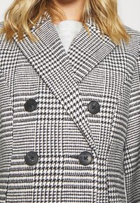 Doppelreihiger Mantel im schwarz-wei�ßen Hahnentrittmuster, mit schwarzen Knöpfen und strukturiertem Stoff. Mit Reverskragen und klar definiertem Schnitt.