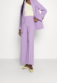 Paarse pak met een op maat gemaakte blazer en een brede pijpenbroek, gecombineerd met een lichtgele top en gele puntige flats. Soepele, lichte stof.