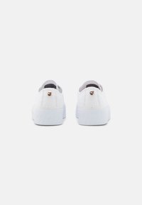 Chaussures blanches en toile à enfiler avec une semelle en caoutchouc blanche texturée. Comprend un petit logo sur le talon. Vue arrière mettant en avant un design simple.