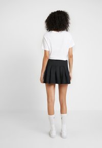 Jupe plissée noire avec une taille ajustée, associée à un t-shirt blanc à manches courtes et des chaussettes de sport blanches. Design minimaliste.