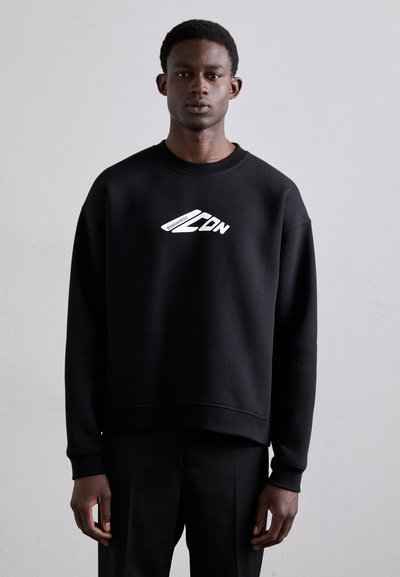 Sweatshirt noir avec un col rond et des poignets côtelés, arborant un texte graphique blanc. Texture lisse, coupe ample et design minimaliste.