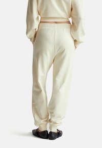 Kremowe dresy wykonane z miękkiego materiału z elastycznym paskiem i ściągaczami, zestawione z czarnymi płaskimi butami z akcentami metalowymi.