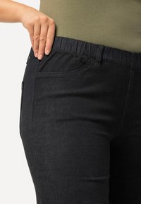 Černé džíny z denimu s elastickým pasem, bočními kapsami a hladkým materiálem. Padnou také těsně, se zaměřením na pohodlí a snadnost nošení.