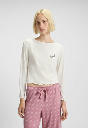 Valkoinen pitkähihainen paita, jossa on aallotettu helma ja "HUGO"-logo. Yhdistetty vaaleanpunaisiin pyjama-housuihin, joissa on toistuva logokuosi ja kiristysnauha.