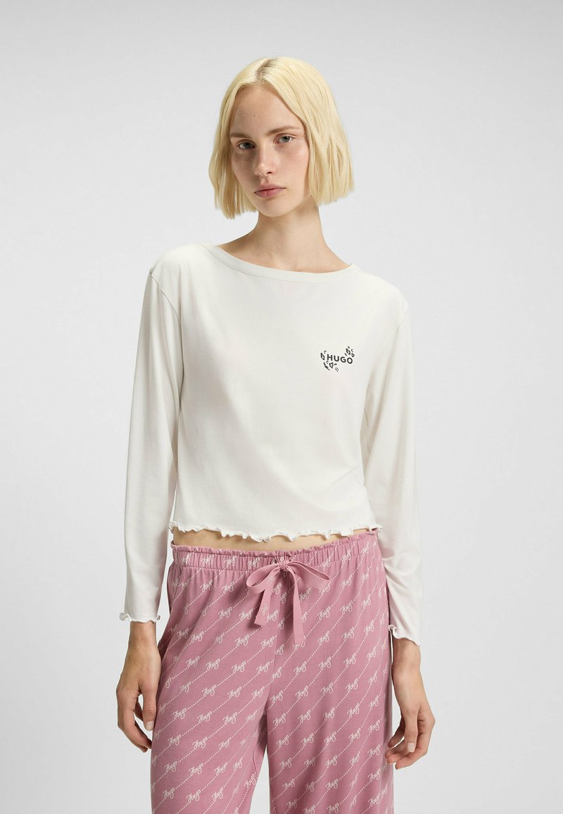 Witte lange mouwen top met een golvende zoom en "HUGO" logo. In combinatie met roze pyjamabroek met een herhaald logo-patroon en trekkoord.