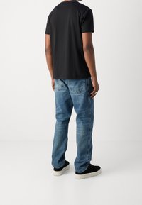 Black cotton t-shirt with short sleeves, paired with blue denim jeans featuring a faded wash and two back pockets. Black sneakers with white soles.