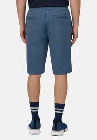 Pantaloncini sportivi blu con vita elasticizzata e due tasche posteriori. Indossati con calzettoni a righe blu navy e scarpe sportive blu.