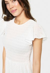 White dress with a textured, smocked bodice and flutter sleeves featuring leaf embroidery. Lightweight and flowy, suitable for warm weather.
