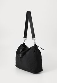 Schwarze Stofftasche mit einer weichen, puffigen Textur. Verfügt über einen Schultergurt und zwei kurze Griffe. Der Reißverschluss ist an der Seite sichtbar.