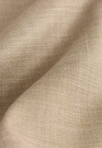 Beige geweven stof met een gestructureerd oppervlak, met een soepele val en fijn, dicht weefpatroon. Zachte, natuurlijke uitstraling van het materiaal.