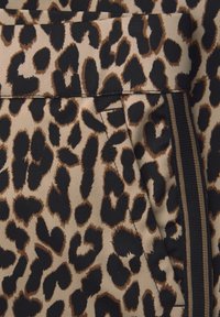 Primo piano di un tessuto con motivo leopardato, caratterizzato da una tasca laterale e da un dettaglio a striscia verticale accanto alla tasca.