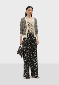 Crna i krem odjeća koja sadrži uzorčastu kardigan, bluzu s točkicama i široke hlače. Dodaci uključuju teksturiranu torbu i naušnice.