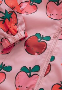 Rosa Jacke mit glänzender Oberfläche, die mit roten und grünen Obstmustern versehen ist. Elastische Bündchen und ein Reißverschluss vorne.