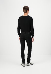 Black long-sleeve top and black skinny jeans, paired with white and black sneakers, viewed from the back against a plain background.