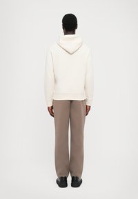 Kremfarget hettegenser med snor og kengurulomme, kombinert med grå avslappede bukser og svarte joggesko. Glatt stoff, tilfeldig design.
