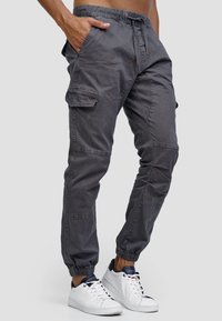 Graue Cargo-Hosen mit einem Kordelzugbund, zwei Seiten Taschen und gerafften Bündchen, hergestellt aus einem weichen, strukturierten Stoff.