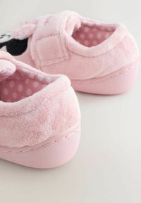 Pink plush slippers with a textured exterior, polka dot lining, adjustable strap, and a smooth pink sole. Features rounded shape and soft material.