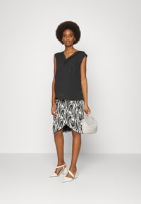 Top preto com detalhe em renda, saia com padrão de zebra, sapatos brancos de salto block, e uma pequena bolsa cinza tecida. Modelo em um fundo neutro.