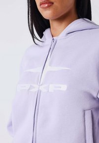 Felpa con zip di colore viola chiaro, realizzata in morbido tessuto, caratterizzata da una stampa bianca del logo e due tasche laterali. Design del cappuccio notevole con vestibilità comoda.