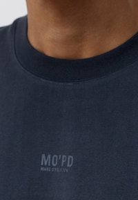 Námořnická modrá bavlněná trička s kulatým výstřihem, s malým tištěným logem "MO'PD" na levé straně, hladká textura a standardní střih.