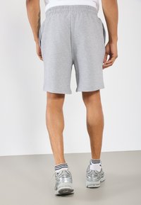 Shorts en coton gris avec une taille élastique, des poches latérales et une coupe décontractée, associés à des chaussures de course argentées et des chaussettes rayées.