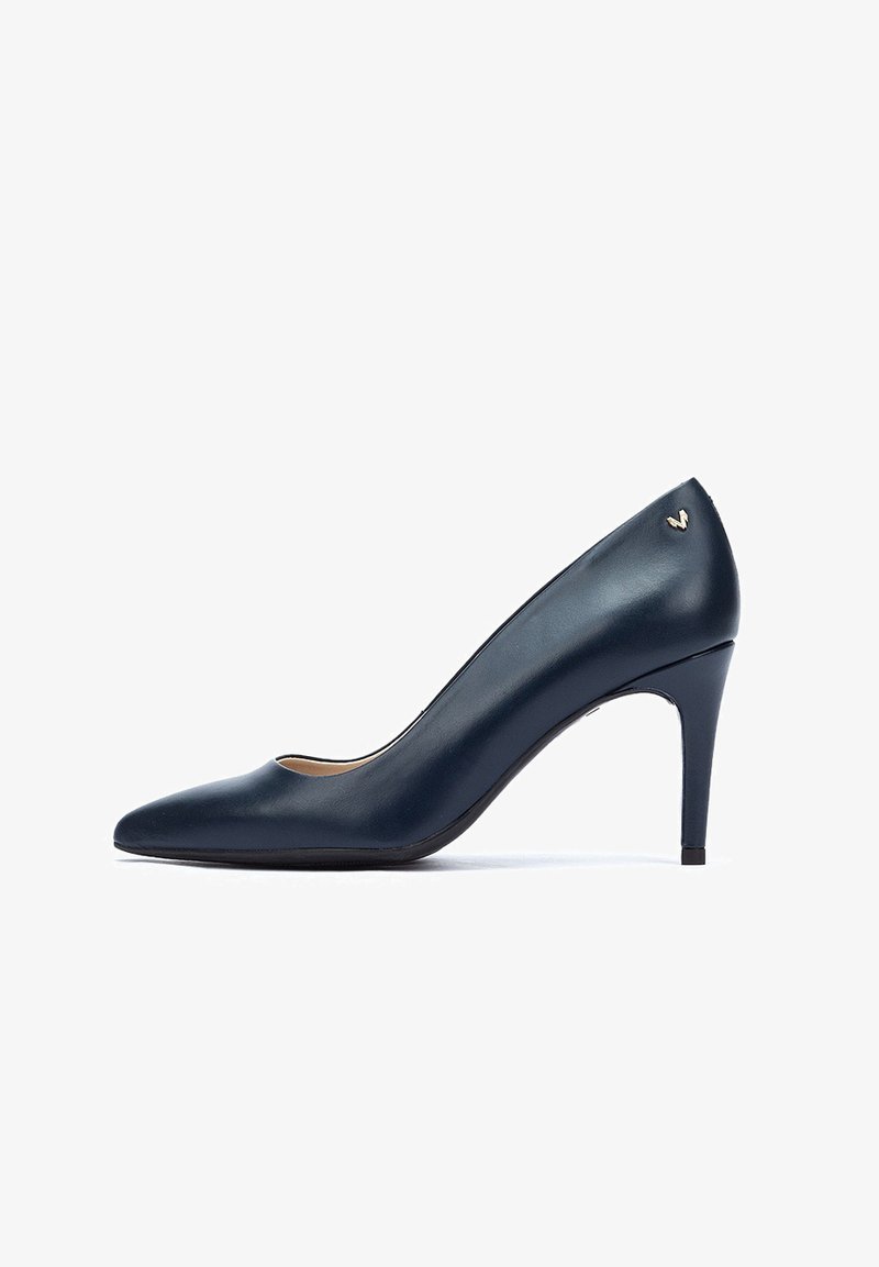 Pump in pelle blu navy con tacco alto e punta affilata. Presenta un piccolo dettaglio del logo dorato sul retro. Texture liscia.