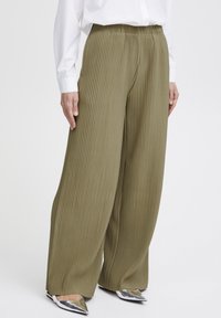 Pantaloni ampi verde oliva con pieghe verticali. Vita elastica, tessuto leggero, abbinati a scarpe argentate a punta.