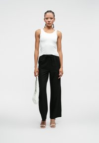 Biały top na ramiączkach, czarne szerokie spodnie i mała biała torebka. Strój charakteryzuje się luźnym krojem i minimalistycznym designem.