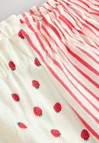 Gros plan sur des ceintures élastiques en tissu blanc à rayures verticales rouges et motifs épars de fraises rouges.