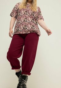 Paita lyhythihaisella kukkakuviolla, jossa on burgundin ja kermaisen sävyjä; yhdistettyinä löysiin burgundinvärisiin housuihin ja mustiin nilkkureihin, joissa on ketjut.