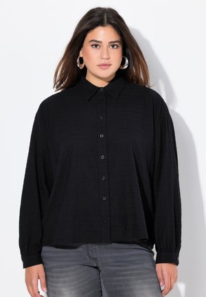Camisa negra de botones con cuello, hecha de tela texturizada. Presenta mangas largas y un corte relajado. Botones en la parte delantera.