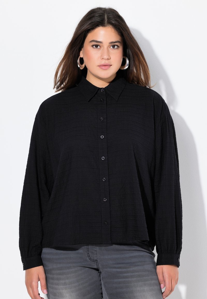Black button-up shirt with a collar, made of textured fabric. Features long sleeves and a relaxed fit. Buttons down the front.