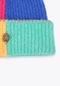 Berretto lavorato a maglia con un design multicolore: sezioni blu, rosa, giallo e verde. Include un accento metallico decorativo sul lato.