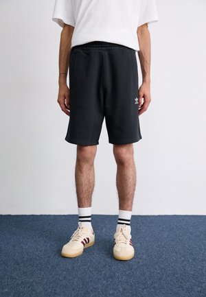 Shorts de sport noirs avec une taille élastique et des poches latérales, associés à des baskets crème avec des rayures bordeaux et des chaussettes blanches avec des bandes noires.