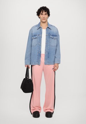 Chaqueta de denim azul claro sobre una camisa blanca, combinada con pantalones de chándal rosas con franjas laterales. Accesorios incluyen un bolso negro y zapatos gruesos.