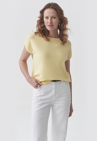 Geel T-shirt met korte mouwen en een ronde halslijn, gecombineerd met witte high waist broek. De stof lijkt glad, lichtgewicht en casual.