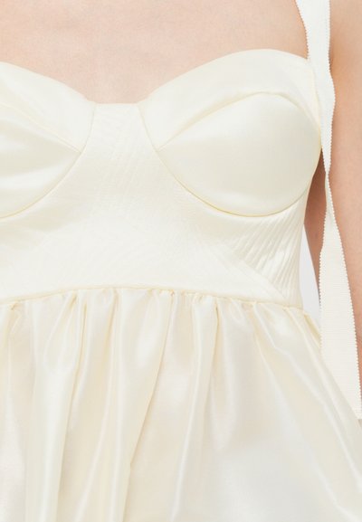 Vestido de satén crema con escote corazón, cuerpo estructurado con patrón acolchado y falda recogida. Incluye finas tirantes en los hombros.