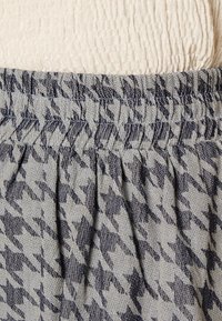 Šedá látka se vzorem houndstooth a námořnickými akcenty; elastický pas se shromážděnou strukturou, vrstvený vzhled.