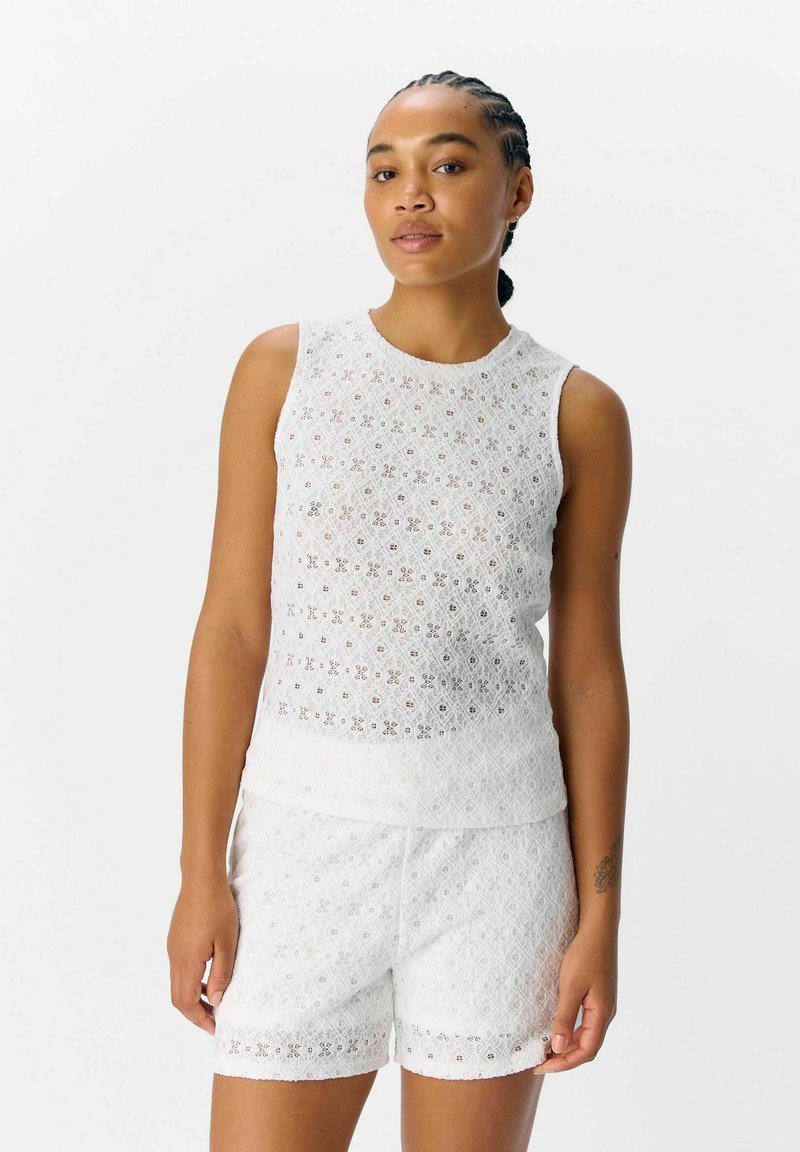 Top de encaje blanco sin mangas con un escote redondo y pantalones cortos a juego. Presenta patrones florales y delicados bordados en toda su superficie.