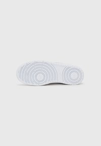 White rubber sneaker sole with circular and linear tread patterns. Contains embossed brand name. Smooth texture, with a rounded toe design.