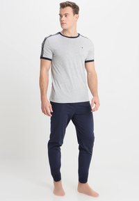 Graues Kurzarm-T-Shirt mit marineblauen Akzenten und Logodetail auf den Ärmeln, kombiniert mit marineblauen Hosen. Glatte Textur und lockerer Schnitt.