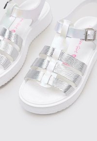 Sandalias metálicas plateadas con un diseño de tiras anchas, superficie texturizada, hebilla ajustable y suela de plataforma blanca.