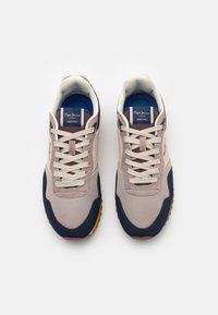 Zapatillas deportivas beige y marino con una parte superior de tela texturizada, punta redonda, cordones en la parte delantera y suelas de goma con acentos naranjas.