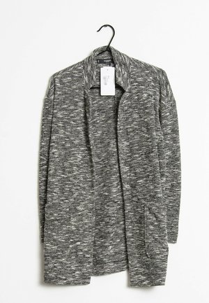 Cardigan gris texturé avec un design à décolleté ouvert, featuring un grand col et deux poches latérales, accroché à un crochet noir.