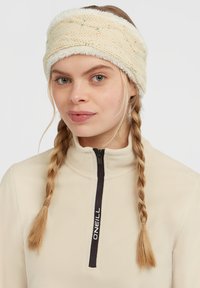 Strikket pandebånd i creme med en blød, pladefoer. Har et struktureret mønster og farveprikker. Designet til varme og komfort.
