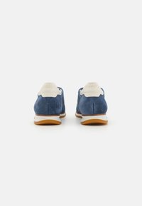 Zapatillas de ante azul con un talón color crema y lengüeta a juego, que presentan una suela blanca y acentos texturizados en la parte superior.