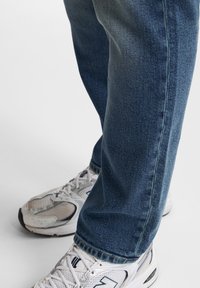 Jeans in denim blu con un taglio dritto, caratterizzati da un lavaggio chiaro e una cucitura sottile. Abbinati a sneakers bianche da ginnastica.