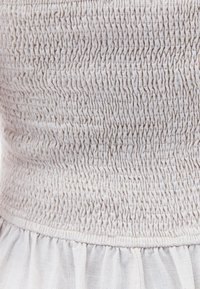 Ljusbeige smockad tyg med en rynkad textur, med en samlad midja och en flödande, mjuk kjoldel nedanför.