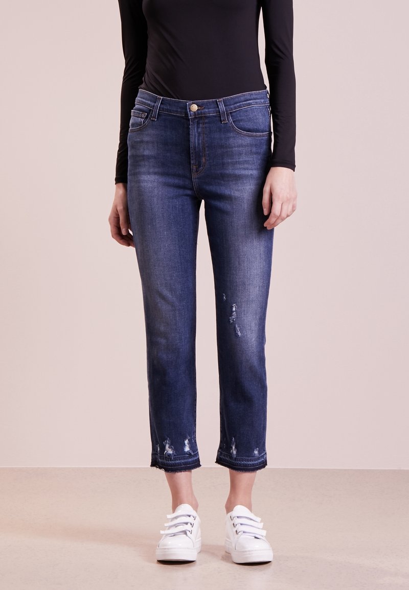Jean en denim bleu foncé, slim fit, légèrement délavé, longueur coupée et ourlet fini. Assorti avec des baskets blanches.